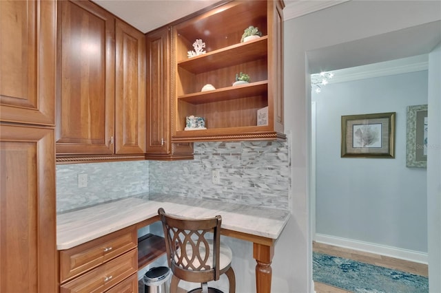 office area with built in study area, baseboards, ornamental molding, and wood finished floors
