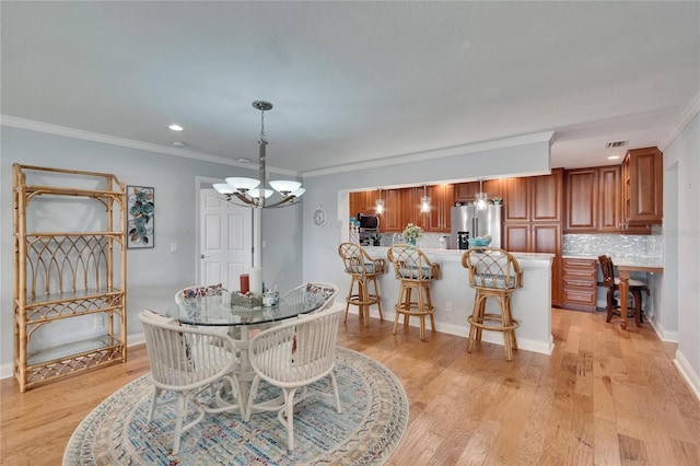 dining room with an inviting chandelier, light wood-type flooring, ornamental molding, visible vents, and baseboards