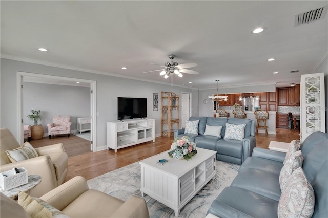 living area with visible vents, crown molding, light wood finished floors, recessed lighting, and ceiling fan with notable chandelier