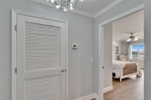 hall featuring a chandelier, light wood-style floors, baseboards, and ornamental molding
