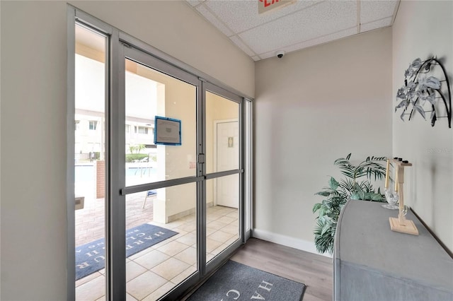 doorway to outside with wood finished floors, baseboards, and a drop ceiling