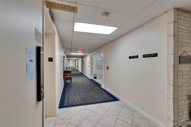 hallway with a drop ceiling, baseboards, and light tile patterned flooring