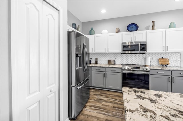 kitchen with tasteful backsplash, light stone counters, gray cabinetry, dark wood finished floors, and appliances with stainless steel finishes