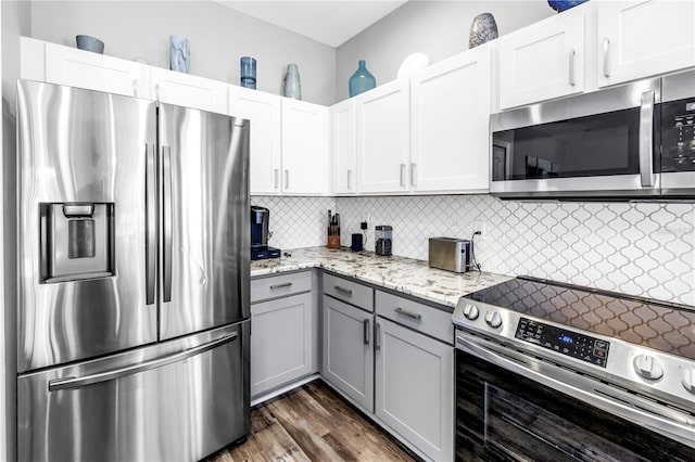 kitchen with gray cabinets, dark wood finished floors, light stone countertops, decorative backsplash, and appliances with stainless steel finishes