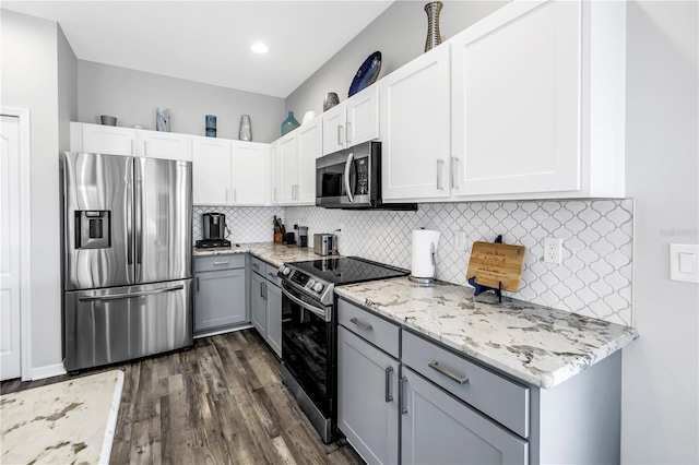 kitchen featuring dark wood-style flooring, gray cabinetry, light stone countertops, decorative backsplash, and stainless steel appliances