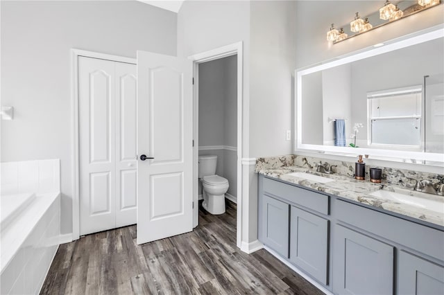 bathroom featuring toilet, a garden tub, wood finished floors, and a sink