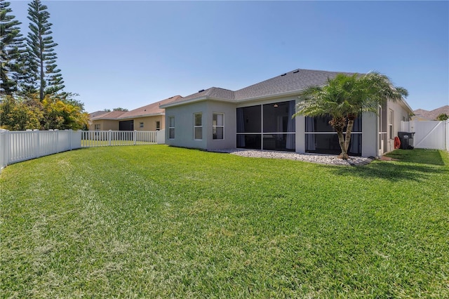 back of property with a fenced backyard, a sunroom, a lawn, and stucco siding