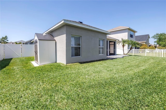 back of house with a lawn, a fenced backyard, an outdoor structure, a storage unit, and stucco siding