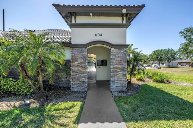 entrance to property featuring a yard, a tile roof, a gate, and stucco siding