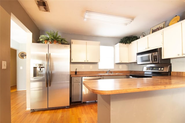 kitchen featuring stainless steel appliances, visible vents, a sink, a peninsula, and light wood-style flooring