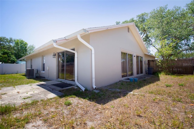 view of side of property featuring stucco siding, fence, and central AC