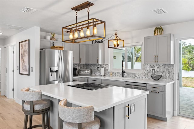 7889 3rd Ave S, Saint Petersburg, FL 33707 - kitchen featuring stainless steel appliances, gray cabinetry, backsplash, light wood-type flooring, and a kitchen island