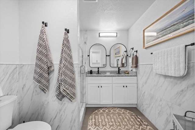 7889 3rd Ave S, Saint Petersburg, FL 33707 - bathroom featuring tile walls, double vanity, toilet, a textured ceiling, and a wainscoted wall