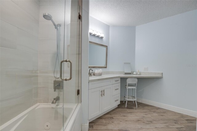 bathroom with wood finished floors, a textured ceiling, combined bath / shower with glass door, vanity, and baseboards