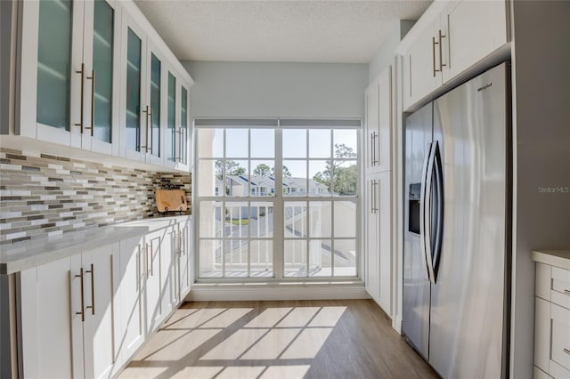 kitchen featuring white cabinets, light wood-style flooring, stainless steel fridge, decorative backsplash, and glass insert cabinets