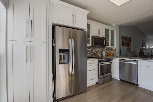 kitchen with white cabinets, light wood-style floors, decorative backsplash, glass insert cabinets, and appliances with stainless steel finishes