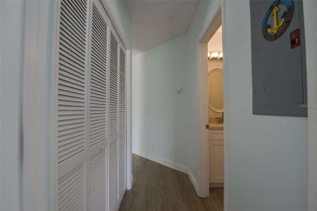 corridor featuring baseboards, wood finished floors, and electric panel