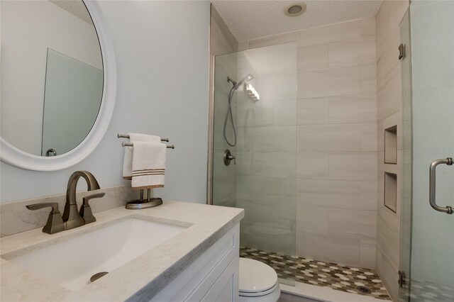 bathroom with vanity, a textured ceiling, a shower stall, and toilet