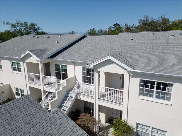 rear view of property with stucco siding, roof with shingles, and stairs