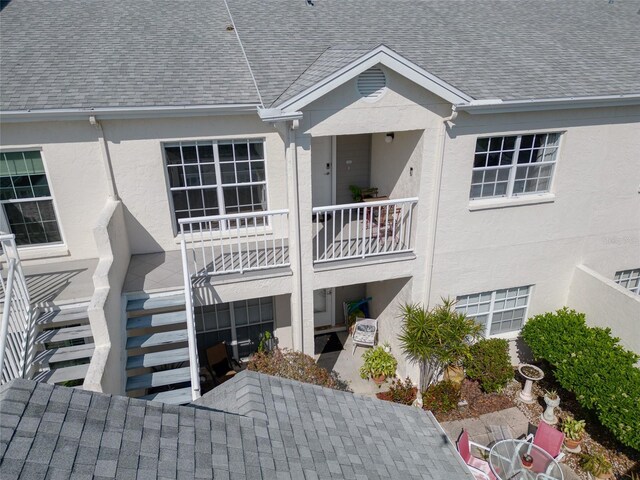 back of house featuring stucco siding, stairway, and a shingled roof