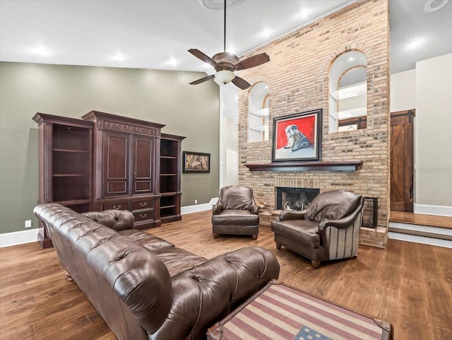living room featuring baseboards, wood finished floors, ceiling fan, and a fireplace