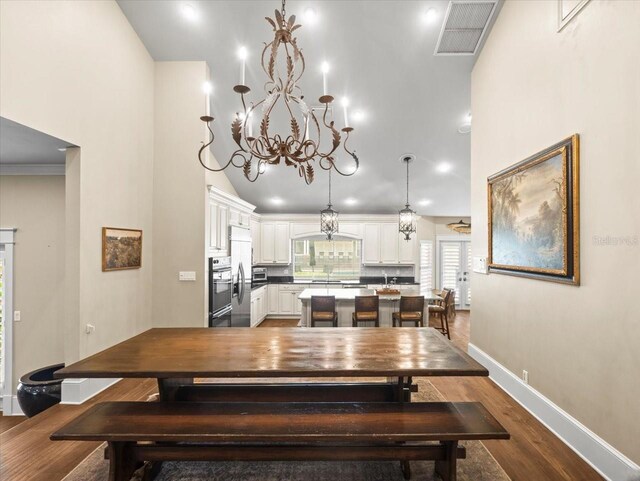 dining space with dark wood-style floors, a chandelier, high vaulted ceiling, visible vents, and baseboards