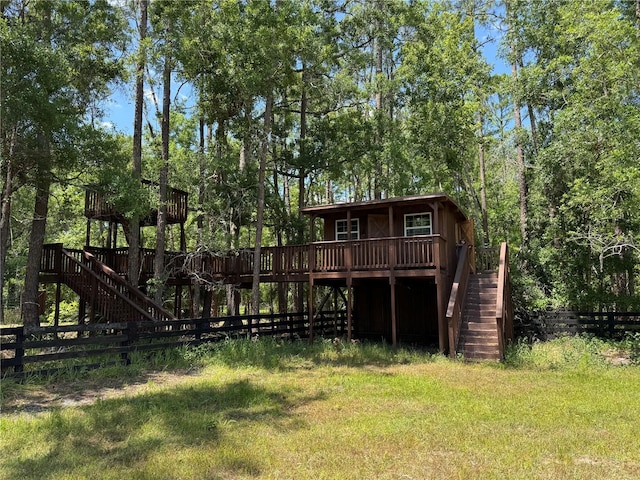 rear view of house with a lawn, stairs, a wooden deck, and fence