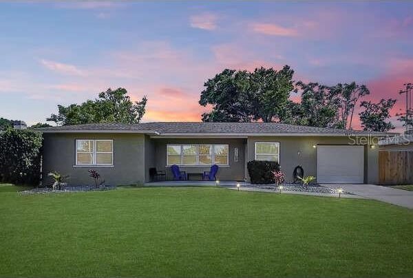 single story home featuring an attached garage, driveway, stucco siding, and a front yard
