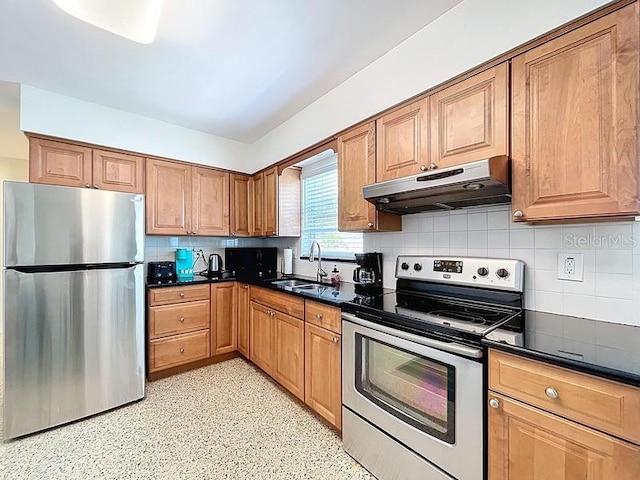 kitchen with appliances with stainless steel finishes, dark countertops, under cabinet range hood, decorative backsplash, and a sink