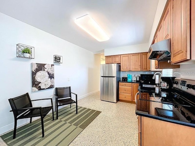 kitchen featuring baseboards, a sink, freestanding refrigerator, under cabinet range hood, and brown cabinetry