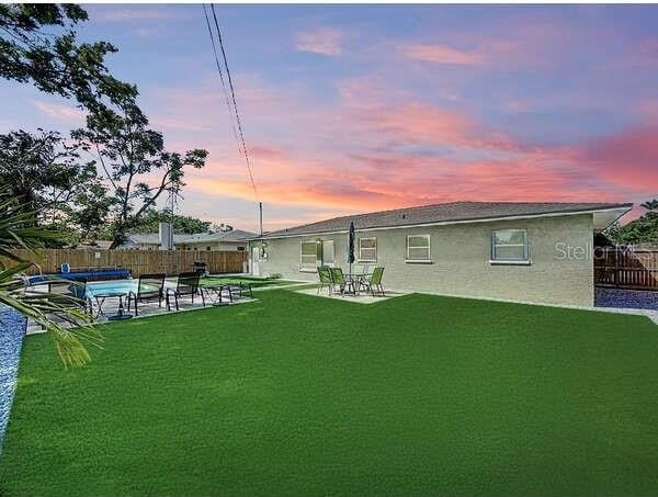back of house at dusk with a fenced in pool, a patio, a fenced backyard, and a lawn