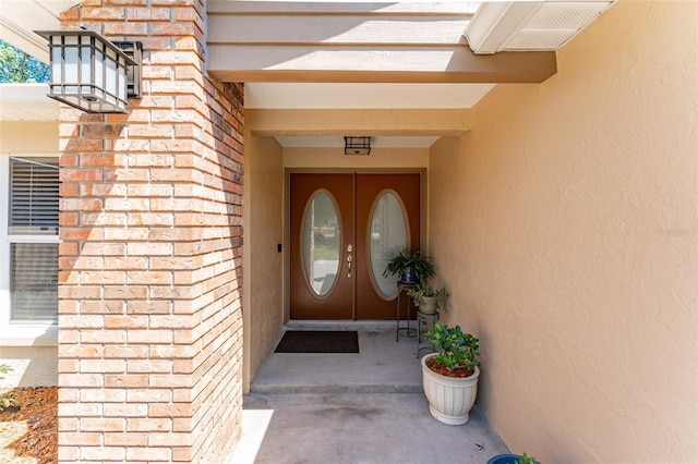 entrance to property featuring brick siding, french doors, and stucco siding