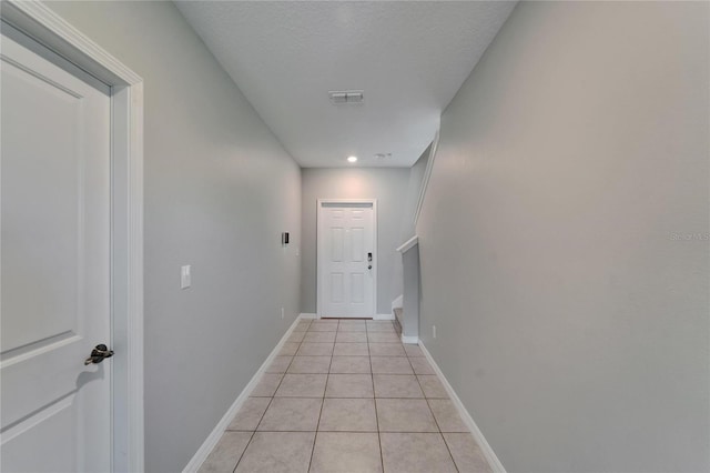 corridor featuring a textured ceiling, visible vents, light tile patterned flooring, stairs, and baseboards
