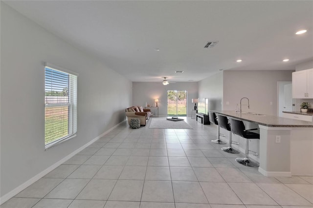 kitchen with open floor plan, light tile patterned flooring, visible vents, a kitchen bar, and a sink