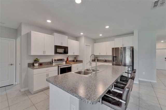 kitchen featuring a kitchen bar, white cabinetry, a kitchen island with sink, a sink, and stainless steel appliances