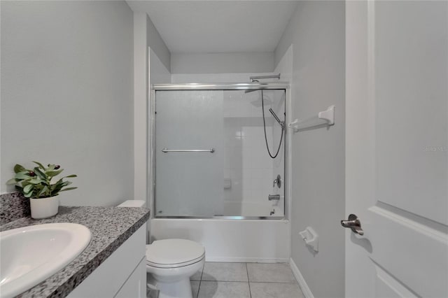 bathroom with combined bath / shower with glass door, vanity, baseboards, tile patterned flooring, and toilet