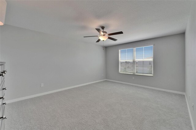 carpeted empty room with baseboards, a ceiling fan, and a textured ceiling