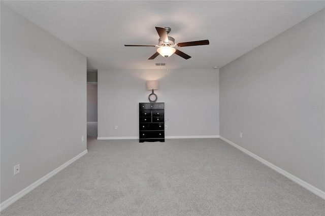 carpeted spare room featuring a textured ceiling, baseboards, a ceiling fan, and visible vents