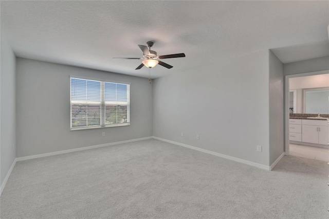 empty room with light carpet, ceiling fan, baseboards, and a textured ceiling