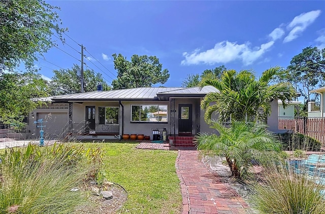 6920 Bougainvilla Ave S, Saint Petersburg, FL 33707 - view of front of home with stucco siding, an attached garage, a front yard, a standing seam roof, and metal roof