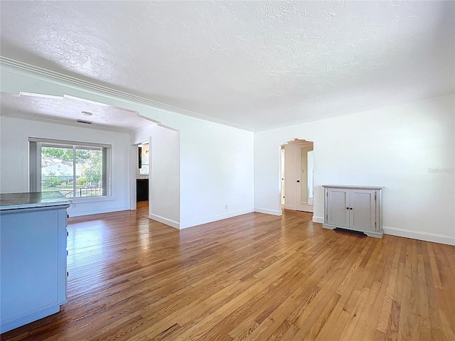 6920 Bougainvilla Ave S, Saint Petersburg, FL 33707 - unfurnished living room featuring arched walkways, light wood finished floors, ornamental molding, and a textured ceiling