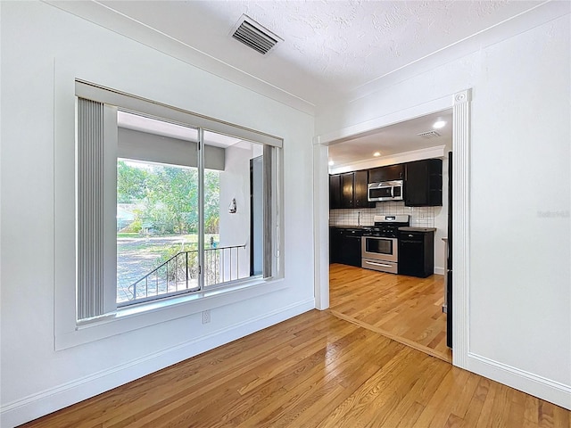 6920 Bougainvilla Ave S, Saint Petersburg, FL 33707 - kitchen featuring visible vents, dark cabinetry, light wood finished floors, stainless steel appliances, and backsplash