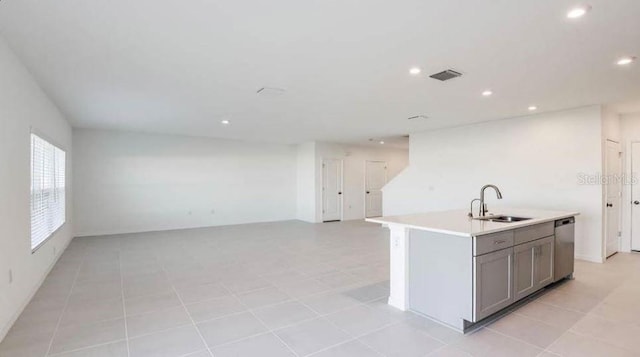 kitchen featuring light countertops, gray cabinetry, a center island with sink, stainless steel dishwasher, and a sink