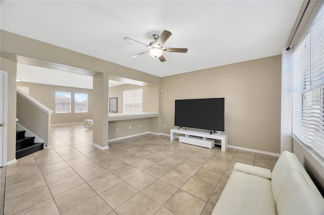 living area with light tile patterned floors, baseboards, a ceiling fan, and stairway