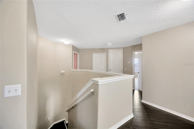hallway with a textured ceiling, visible vents, dark wood-style flooring, an upstairs landing, and baseboards