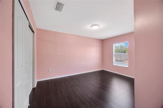 unfurnished bedroom featuring a closet, baseboards, dark wood-style floors, a textured ceiling, and visible vents