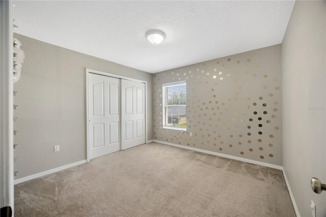 unfurnished bedroom with a textured ceiling, a closet, carpet flooring, and baseboards