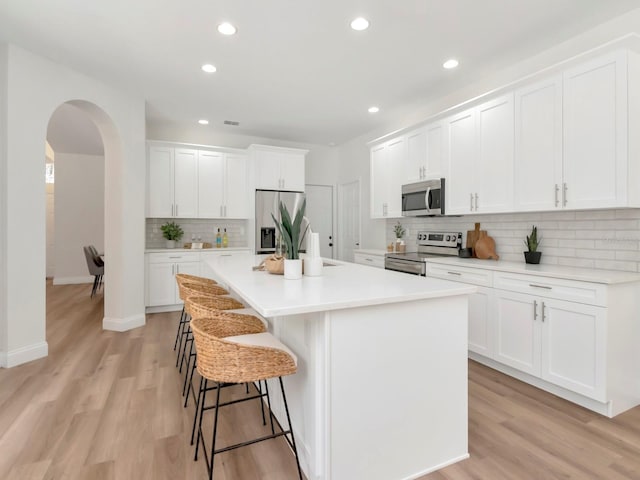 3728 Cypress Meadows Rd, Tampa, FL 33624 - kitchen featuring appliances with stainless steel finishes, arched walkways, a breakfast bar area, a center island, and white cabinets