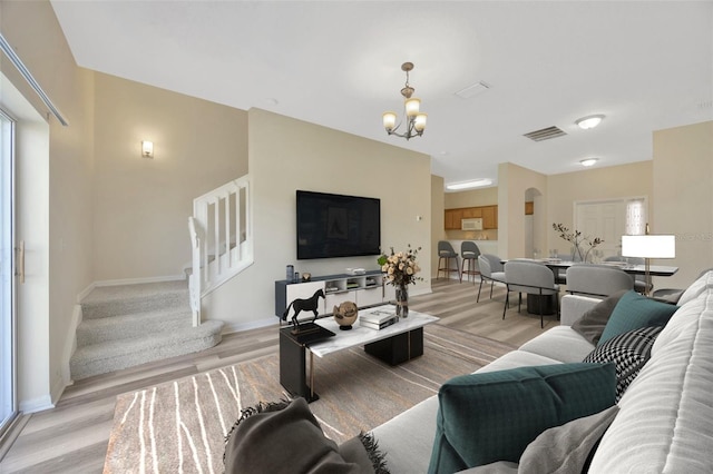living area featuring a notable chandelier, stairway, light wood-style floors, visible vents, and arched walkways