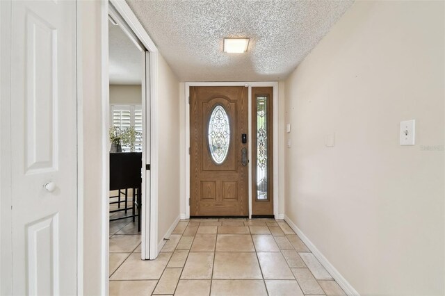 foyer entrance featuring baseboards, a textured ceiling, and light tile patterned floors